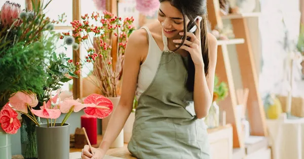 Dueña de una floristería sonríe mientras atiende un pedido por teléfono en el mostrador