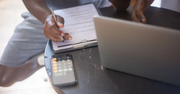 Una persona anota en una planilla junto a una calculadora y una notebook, comparando opciones