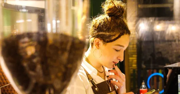 Barista revisa su teléfono entre pedidos en el mostrador de una cafetería